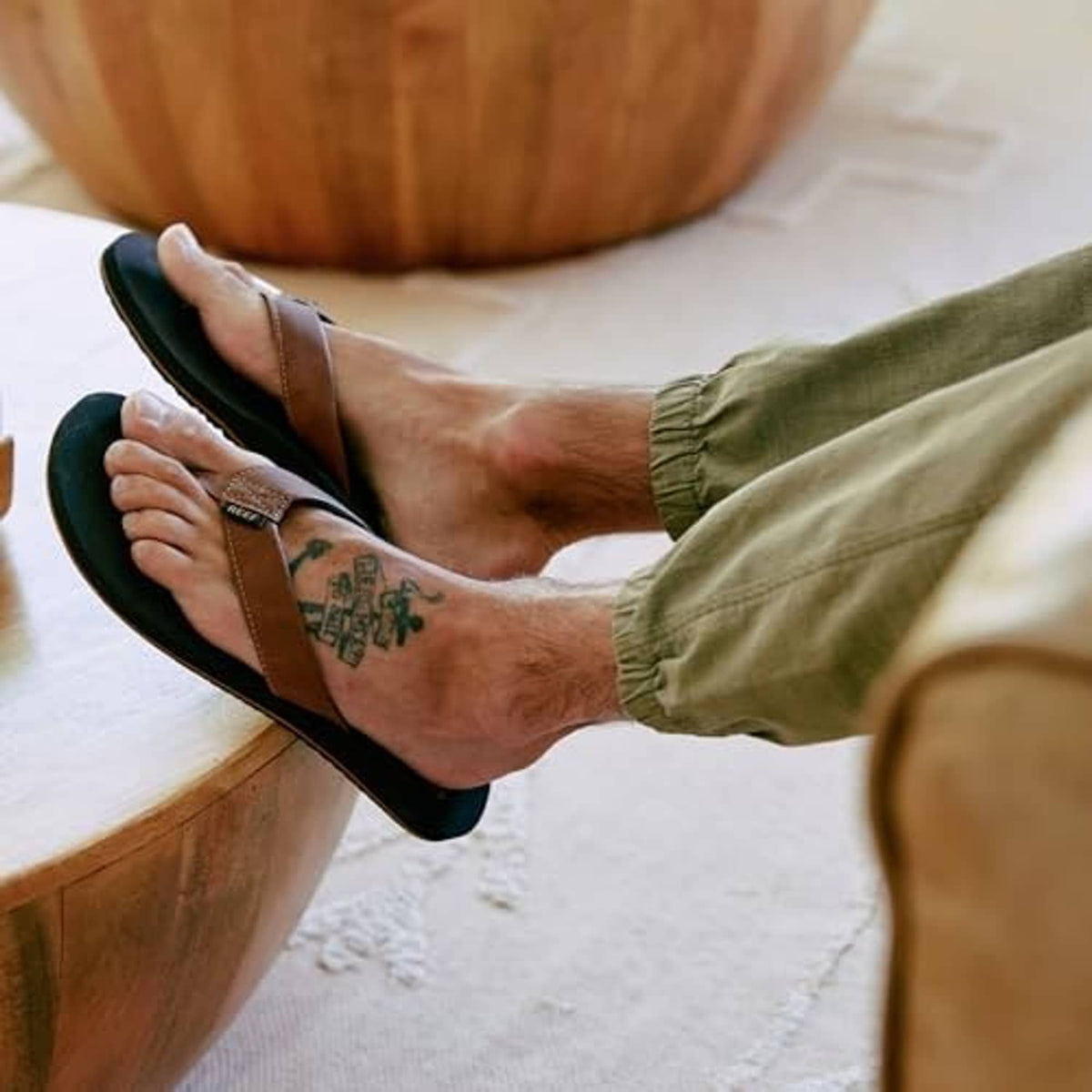 Brown flip-flop sandals with tan thong strap on feet, shown with olive pants.
