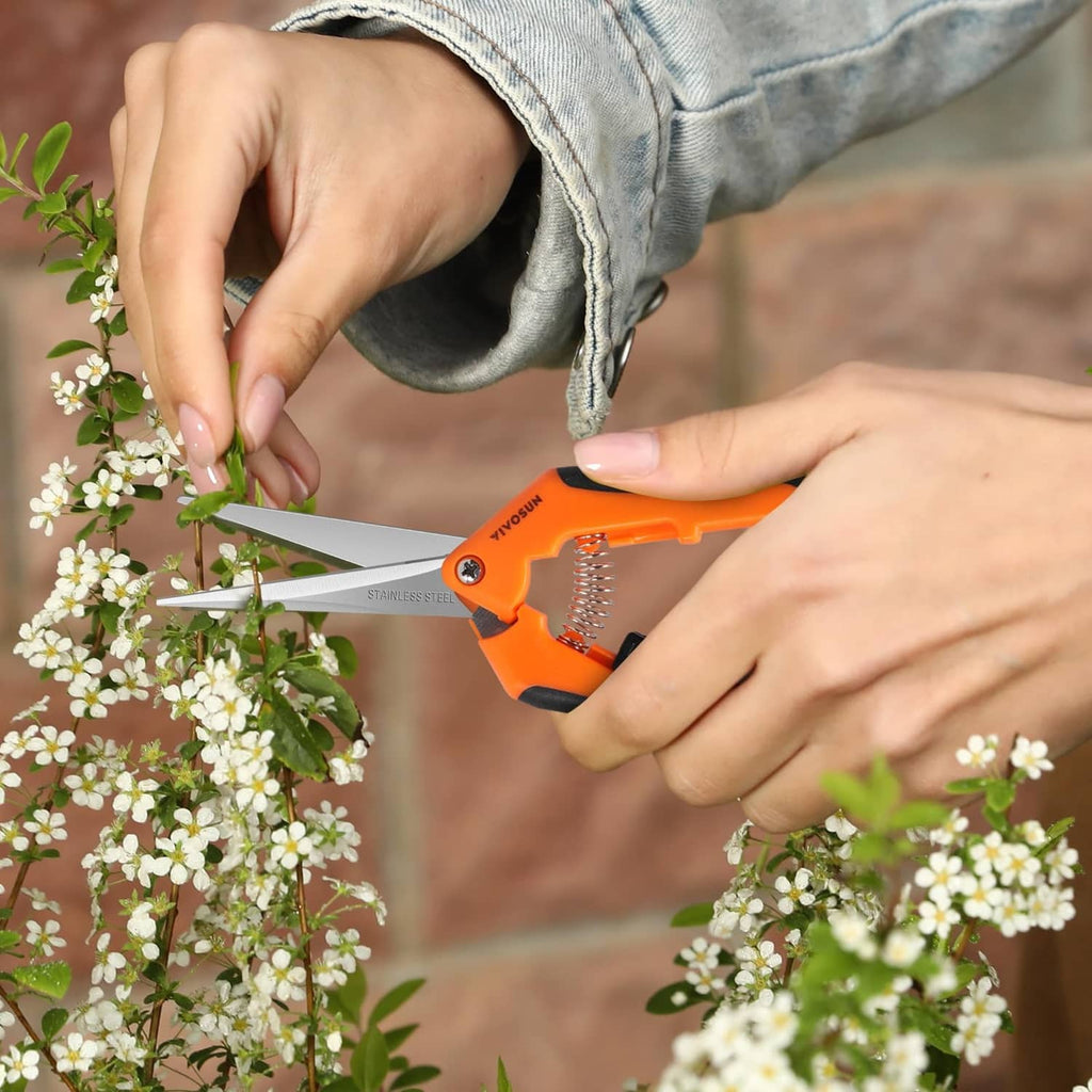 Orange gardening hand pruner cutting white blossoms with stainless steel blades