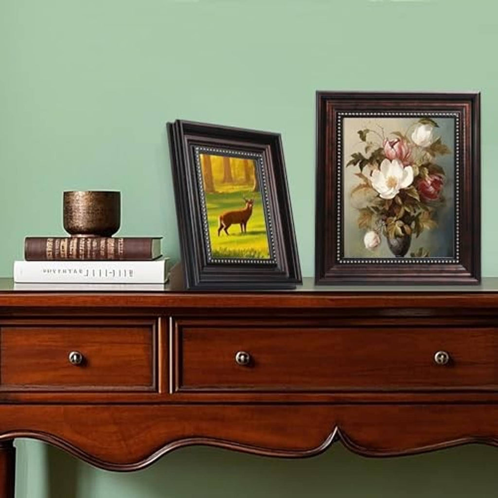 Two vintage black picture frames with gold bead trim on a tabletop, each holding artwork.
