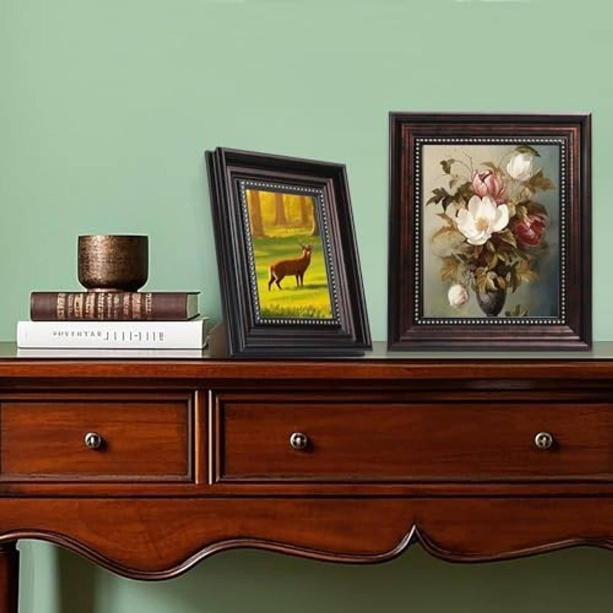 Two vintage black picture frames with gold bead trim on a tabletop, each holding artwork.