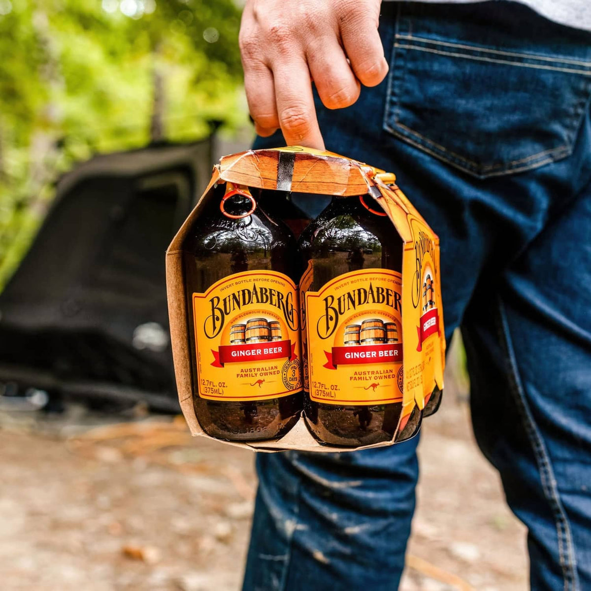 Person holding Bundaberg Ginger Beer 4-pack carrier with four amber bottles