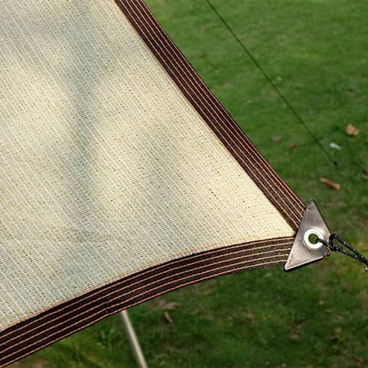 Beige outdoor sunshade cloth with dark striped border and corner fastening on grass