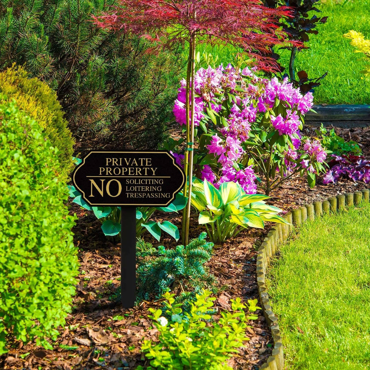Black private property no trespassing yard sign on pointed stake in a garden bed
