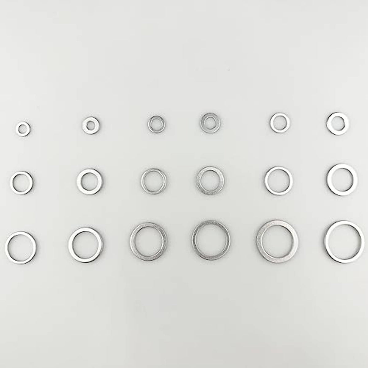 Assorted round aluminum oil drain plug gaskets arranged in rows, silver metal washers