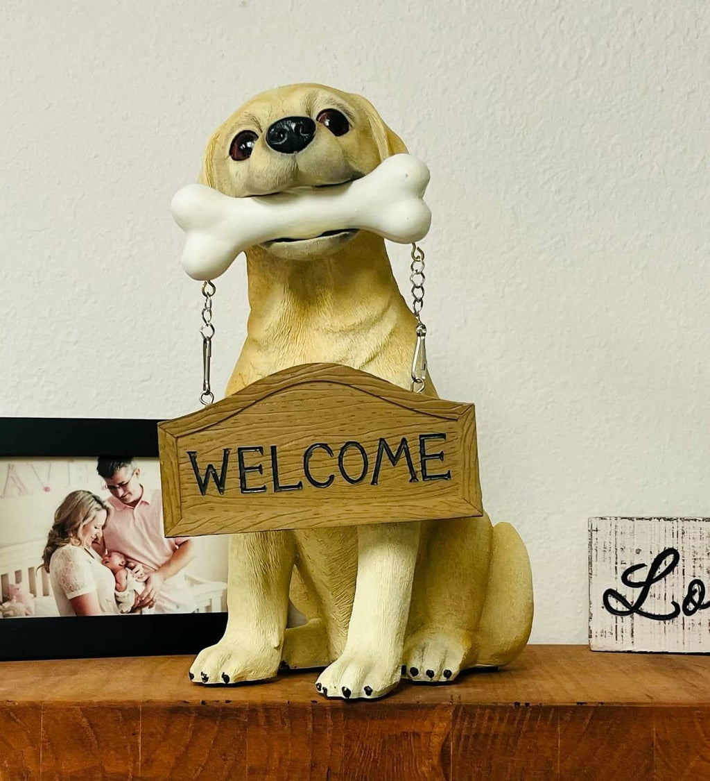 Tan Labrador puppy statue holding a white bone with a “WELCOME” wooden sign
