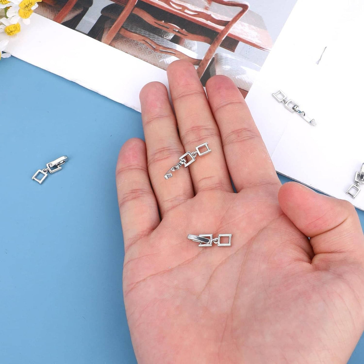 Silver fold-over clasp extender pieces held in palm, small chain clips