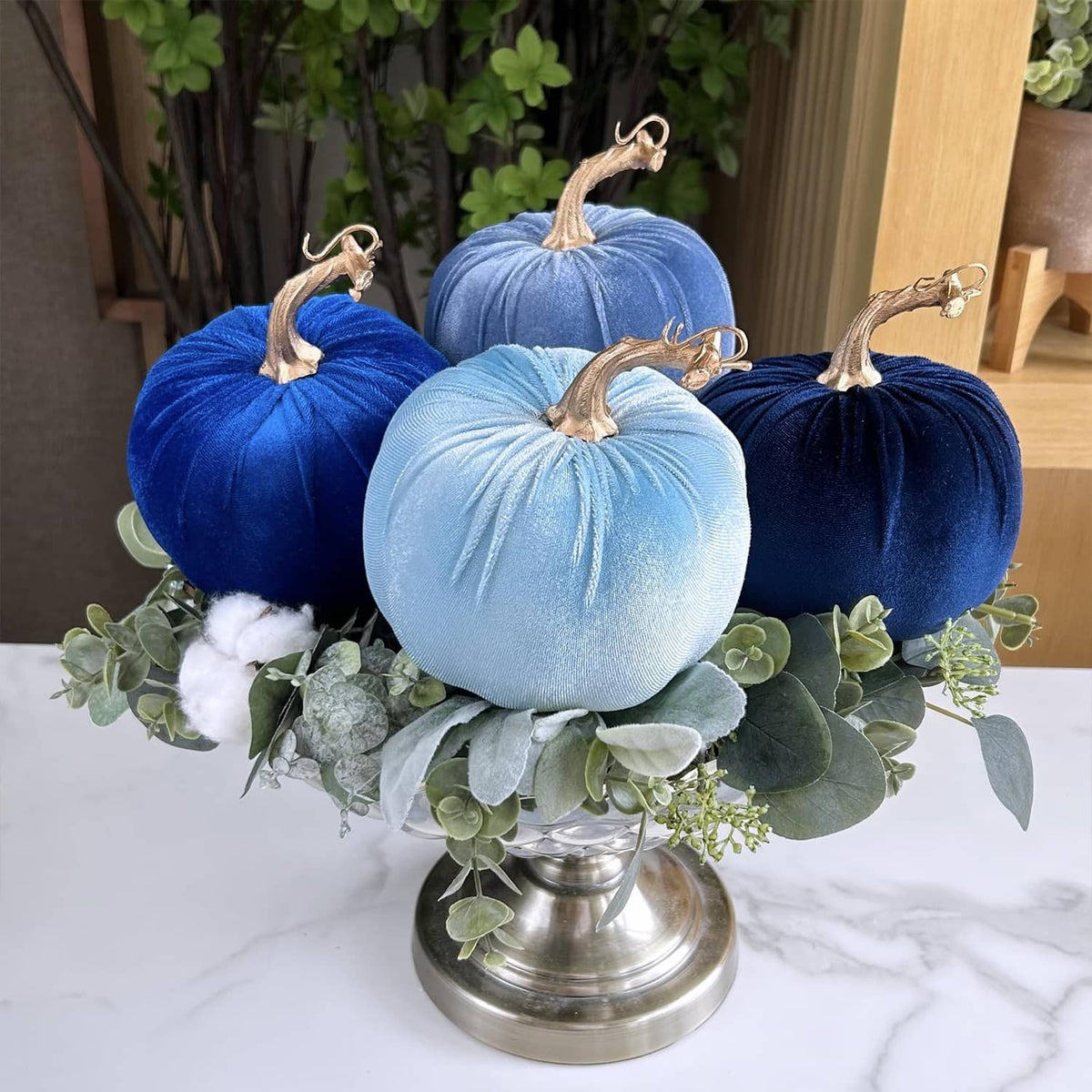 Assorted blue faux velvet pumpkins with gold stems and hanging loops on a metal pedestal