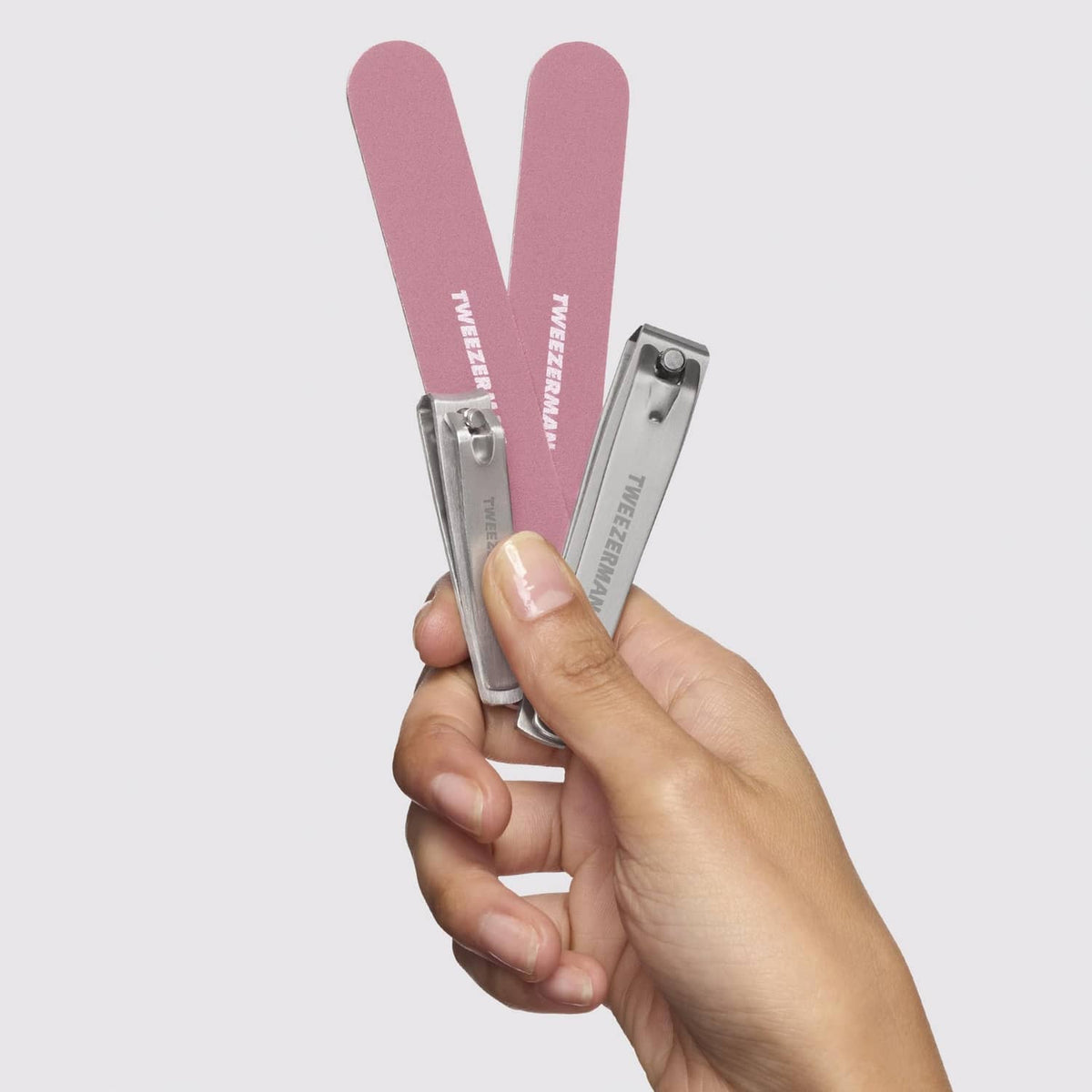 Hand holding Tweezerman nail kit: two rose-pink nail files and silver clippers.