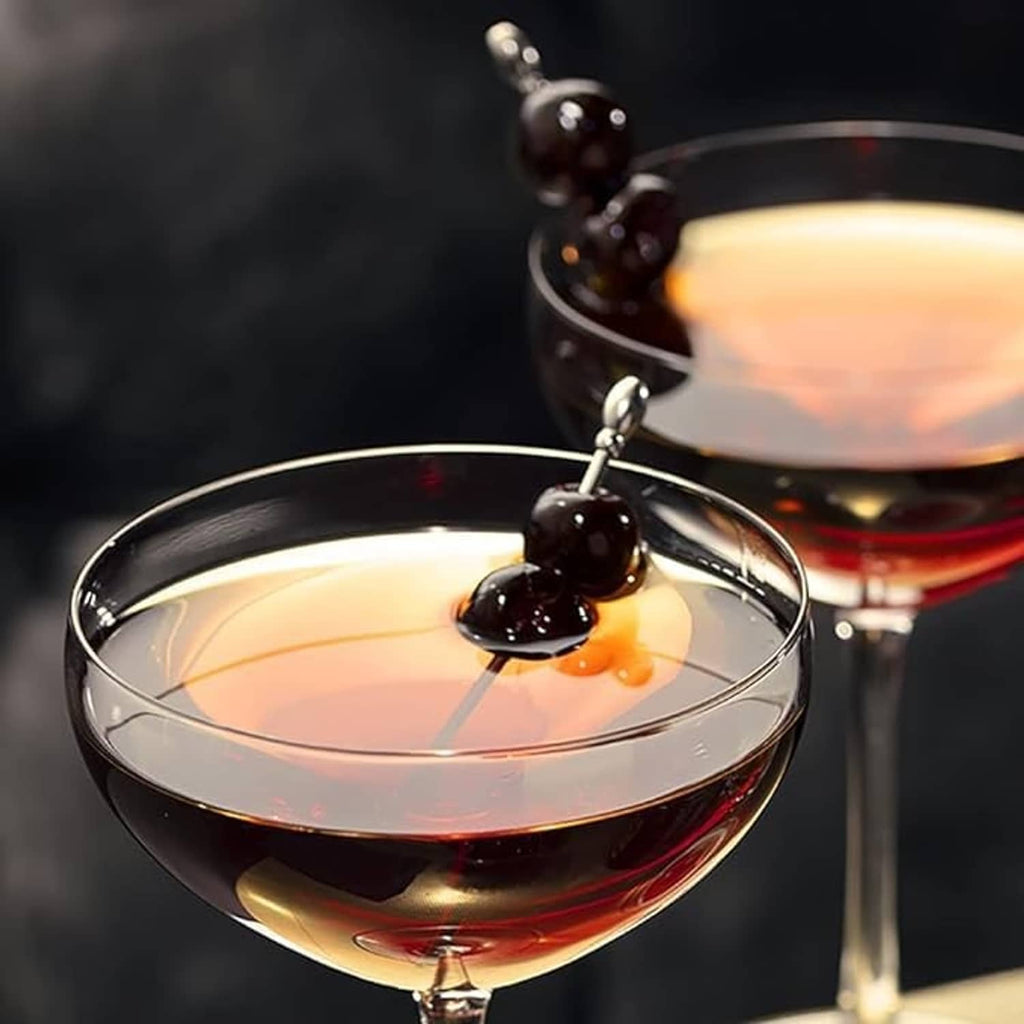 Cocktail glass with floating orange garnish and dark maraschino cherries