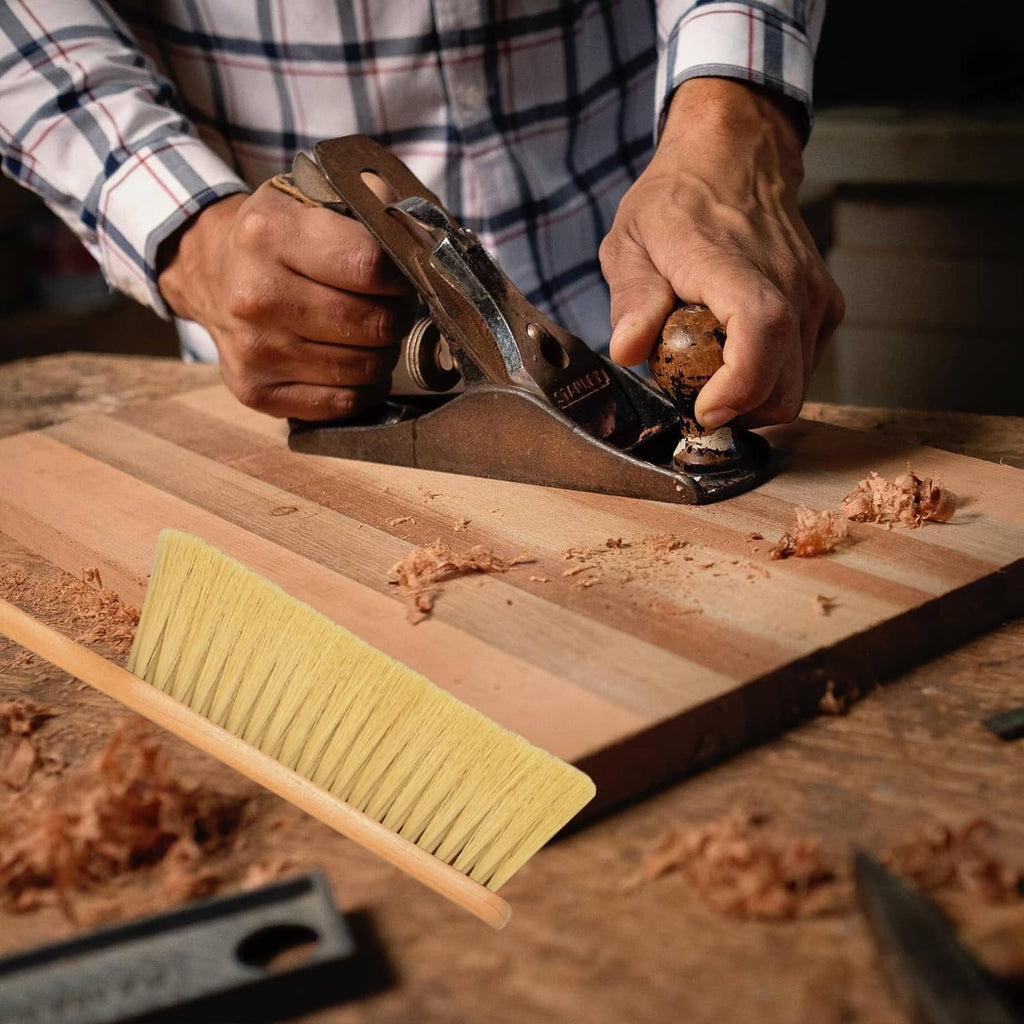 Wooden dust broom with khaki bristles and long handle being used to sweep wood