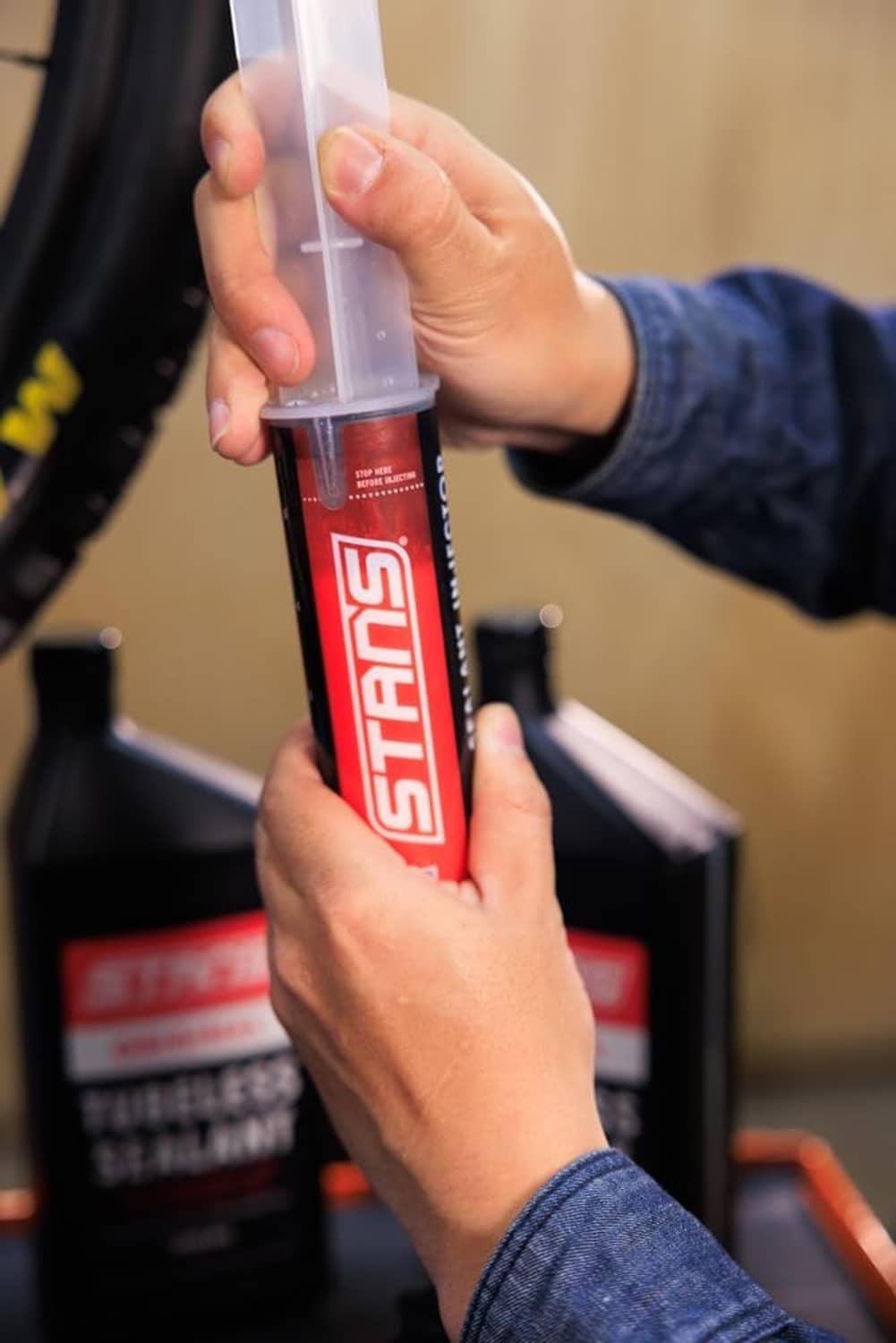 Hands squeezing tubeless sealant injector while dispensing from a clear container