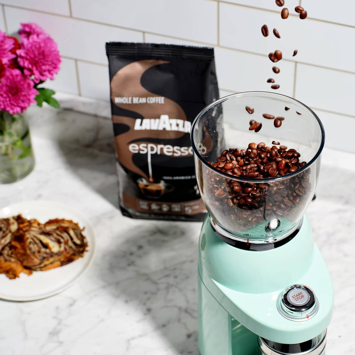 Lavazza espresso whole bean coffee bag beside glass grinder bowl with coffee beans