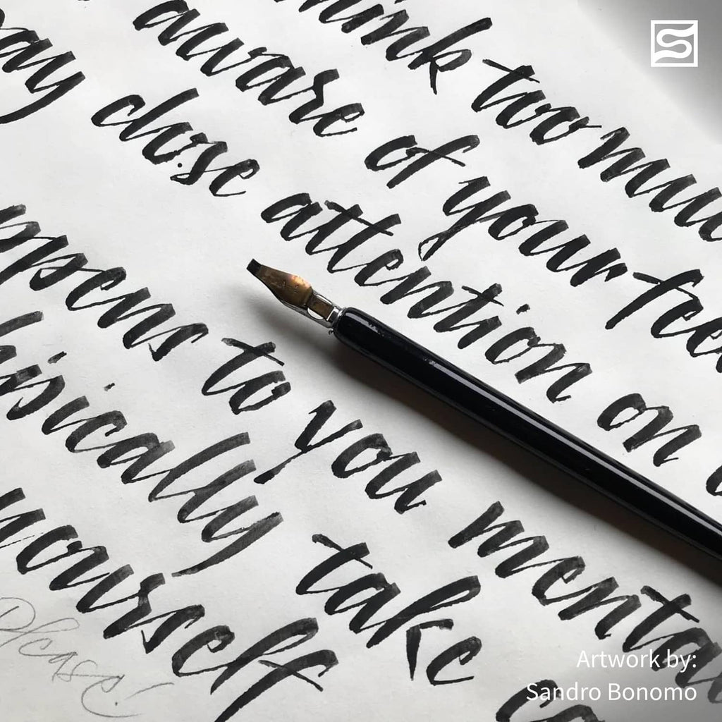 Calligraphy pen applying black ink to paper, close-up of letterforms