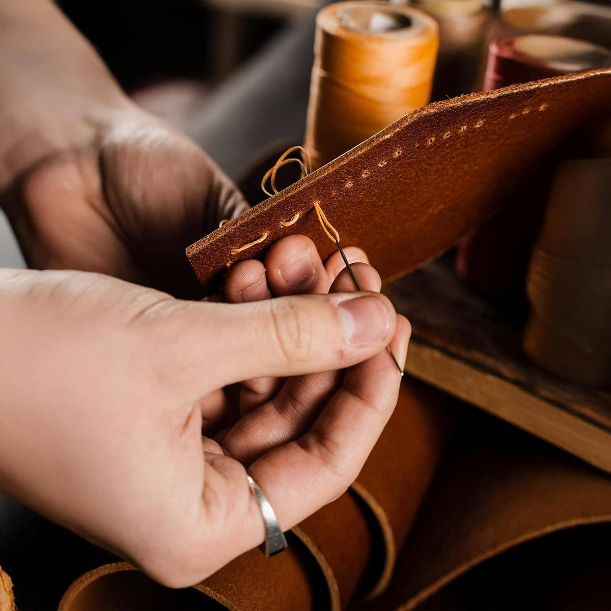 Hand sewing leather with brown waxed thread using a needle and awl