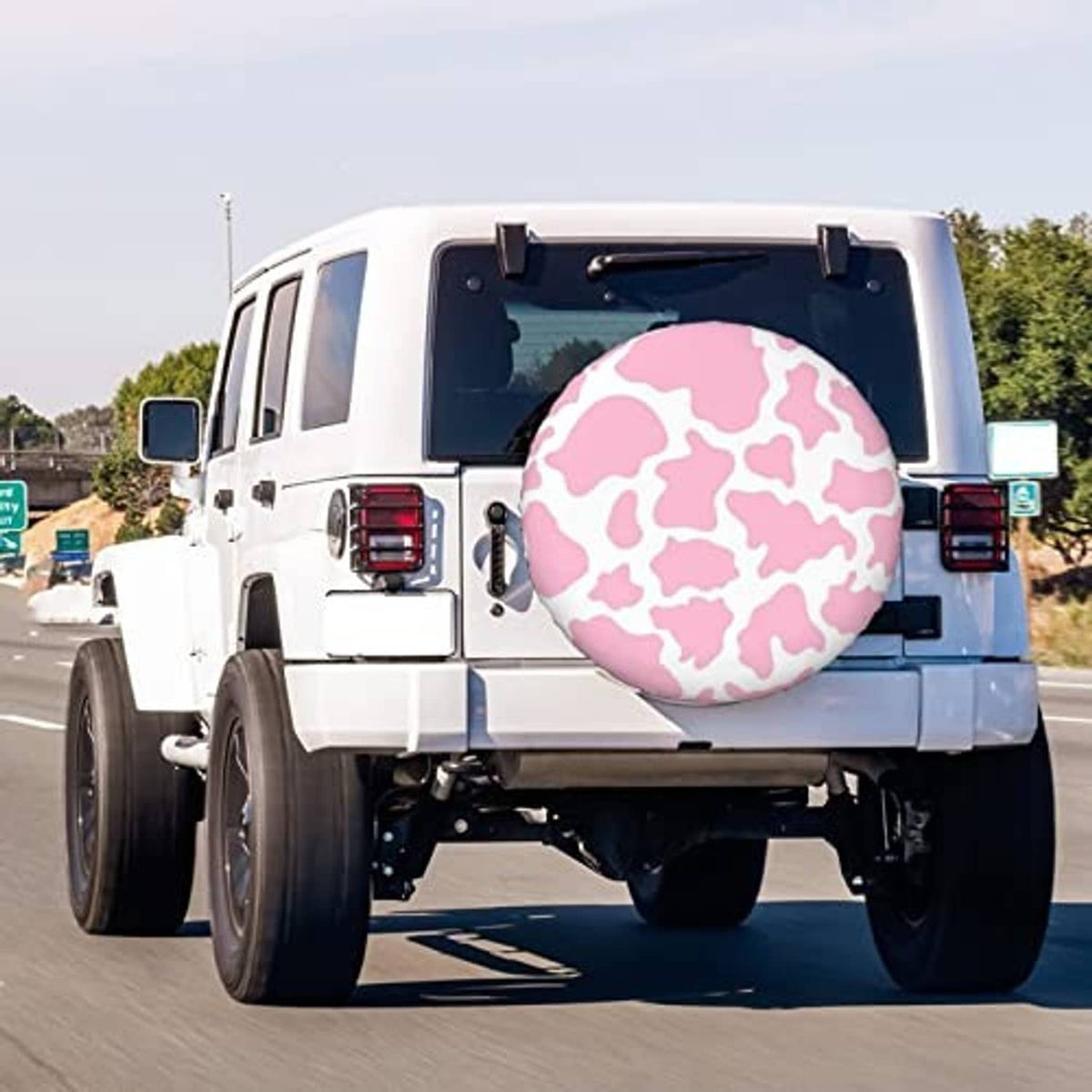 Pink cow-print spare tire cover on a white SUV, round cover with black outer edge