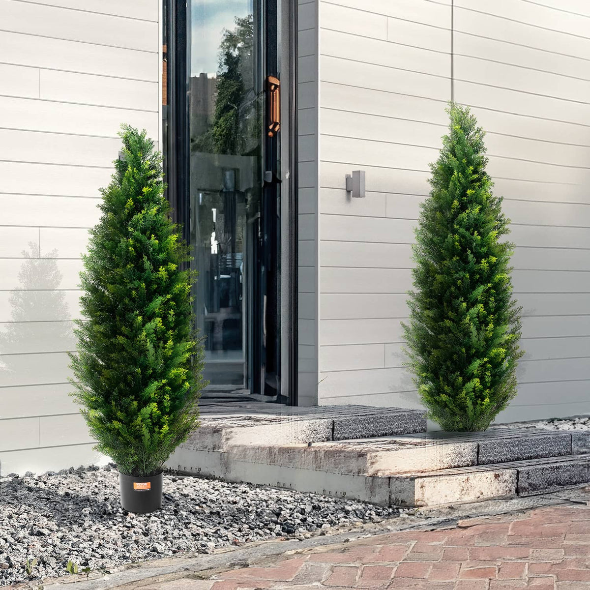 Two artificial cedar topiary trees in black pots near an exterior doorway
