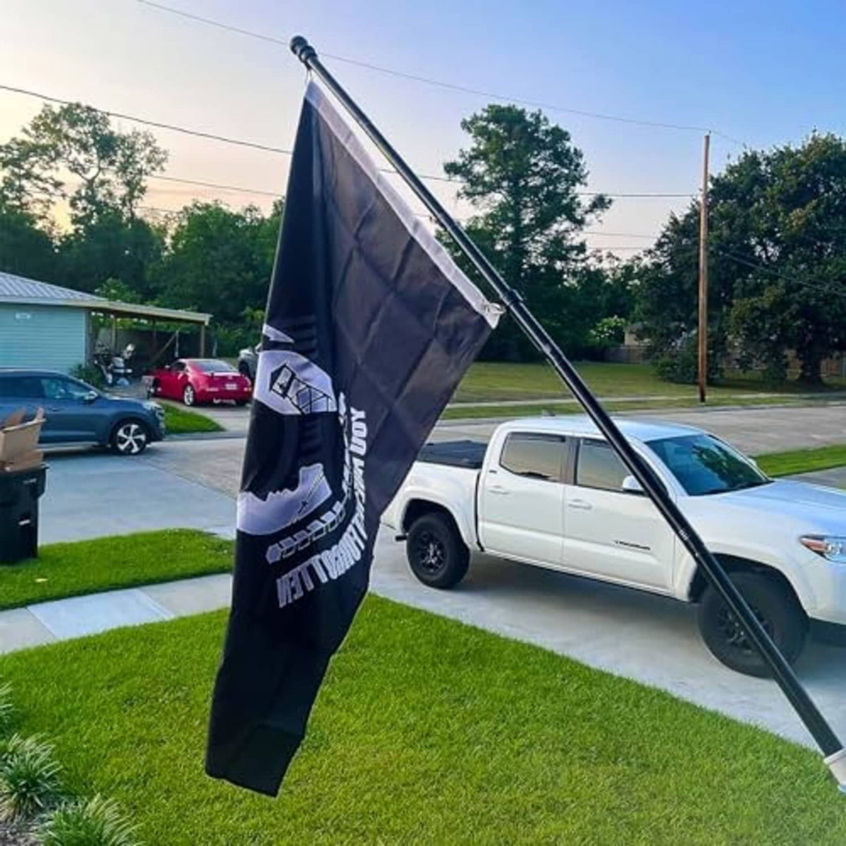 Black POW*MIA embroidered flag hanging on metal pole outdoors, circular silhouette and motto