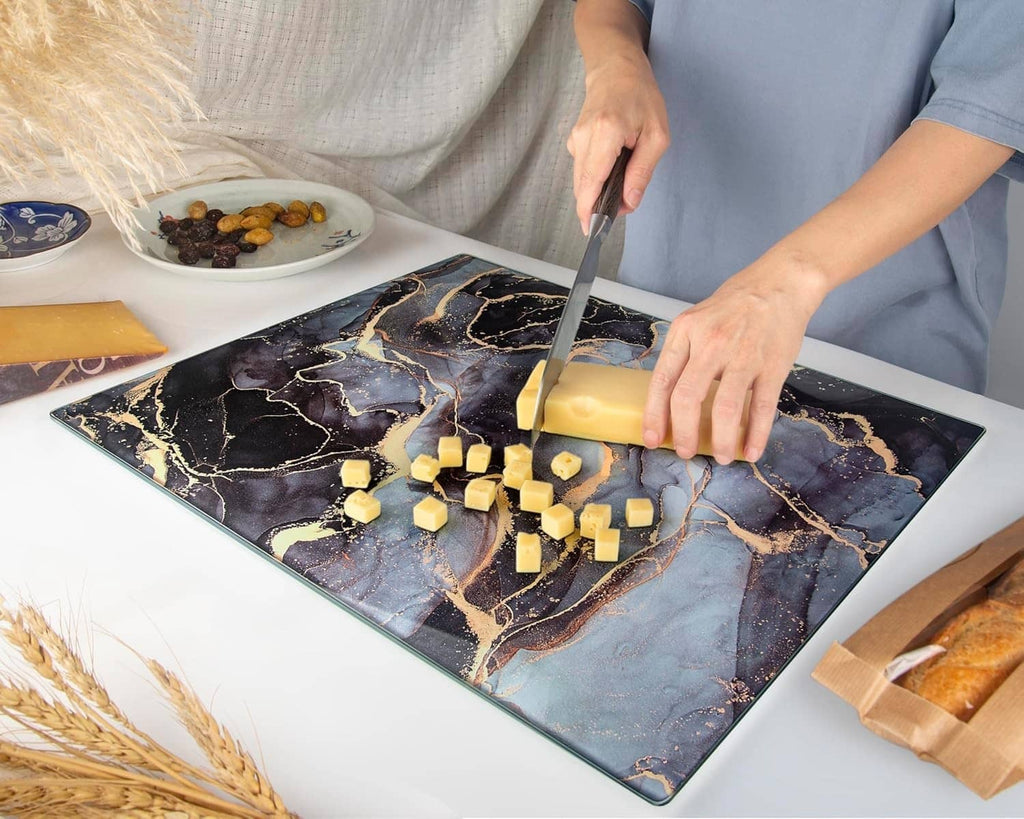 Tempered glass cutting board with blue and gold marbled pattern, cheese being chopped