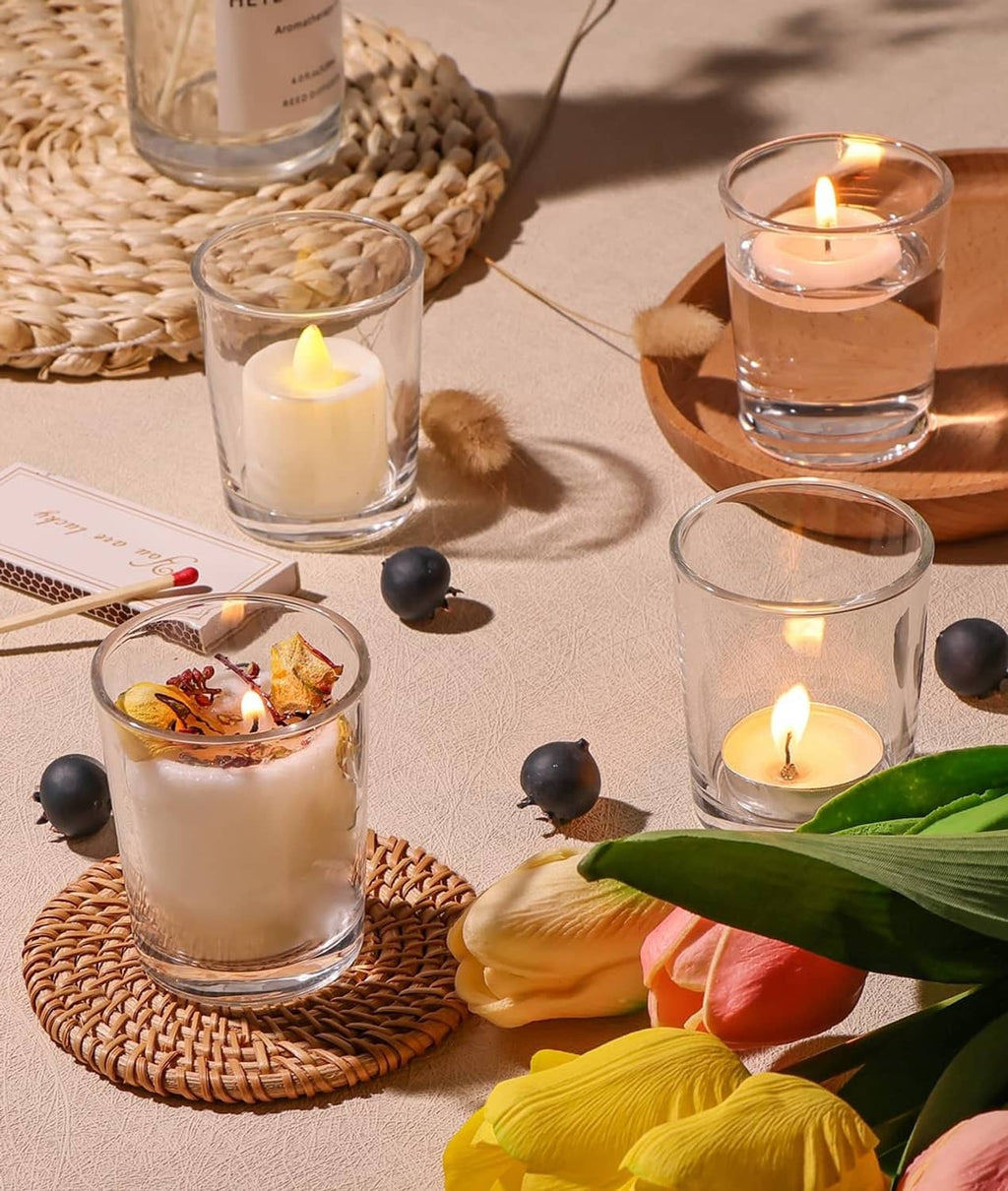 Clear glass tea light holders with lit candles beside flowers and greenery