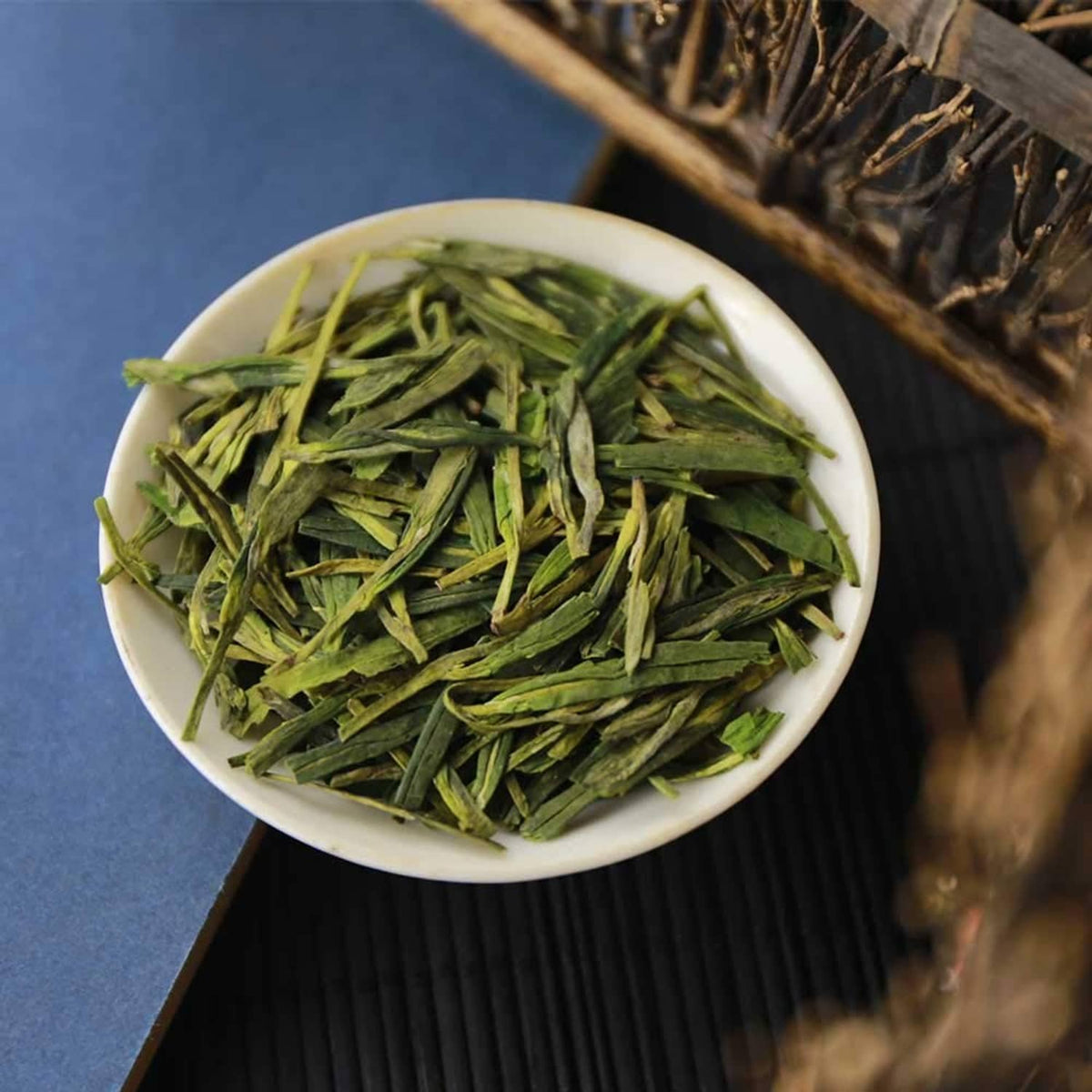 Loose green tea leaves in white bowl on a dark tea mat