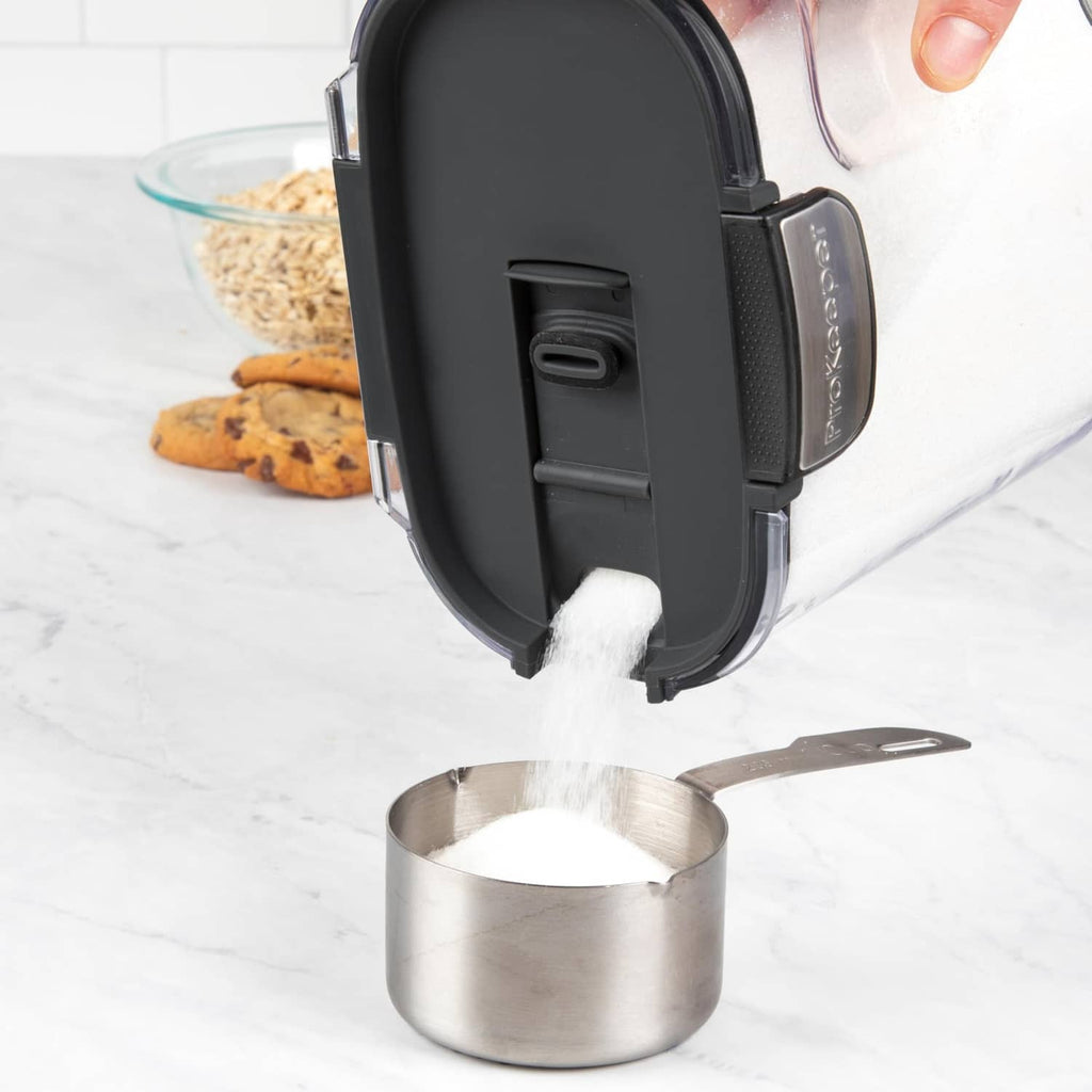 Pouring from clear airtight container into metal measuring cup, black flip-top lid
