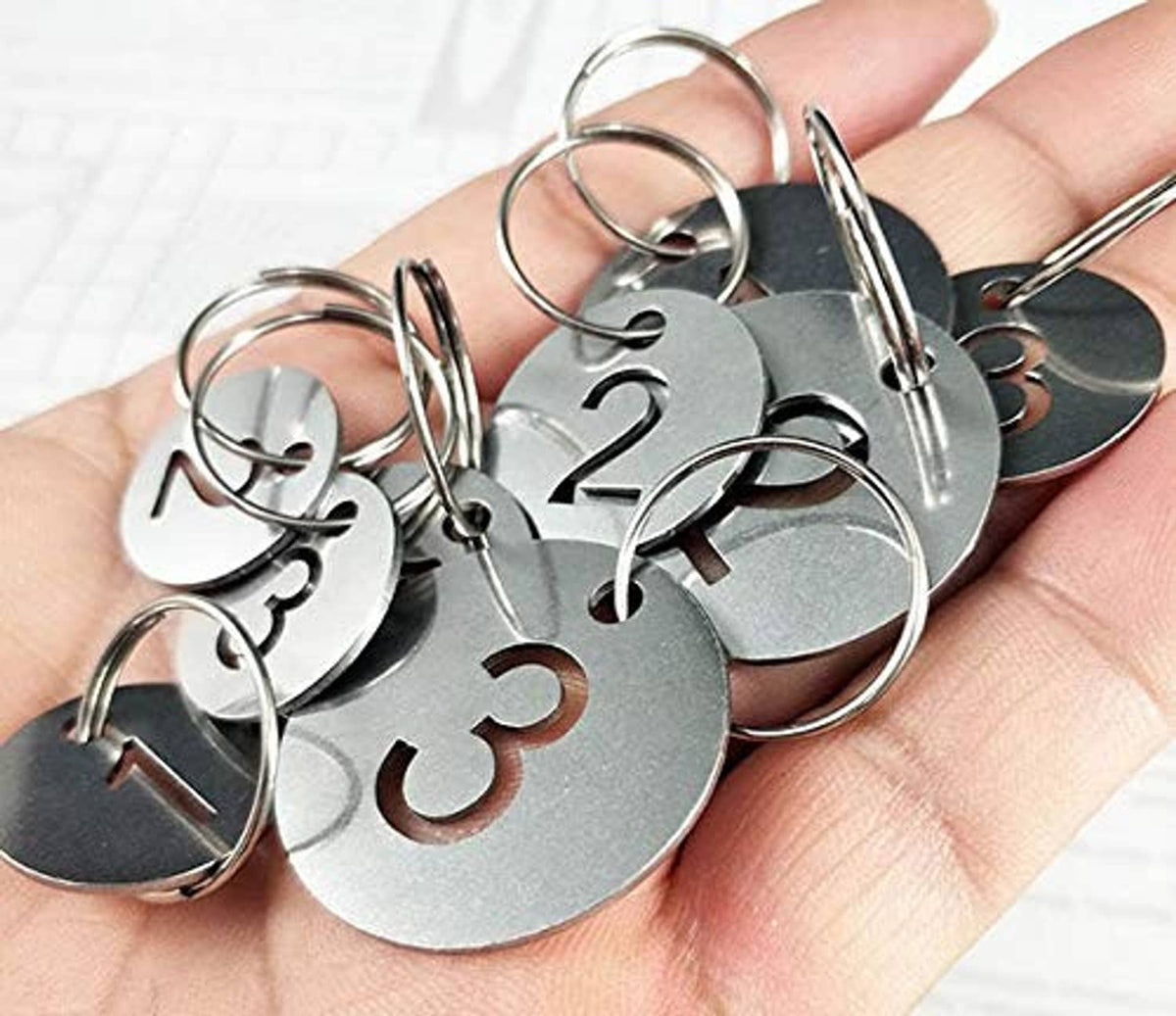 Stainless steel number key tags with rings held in hand, showing multiple numbers