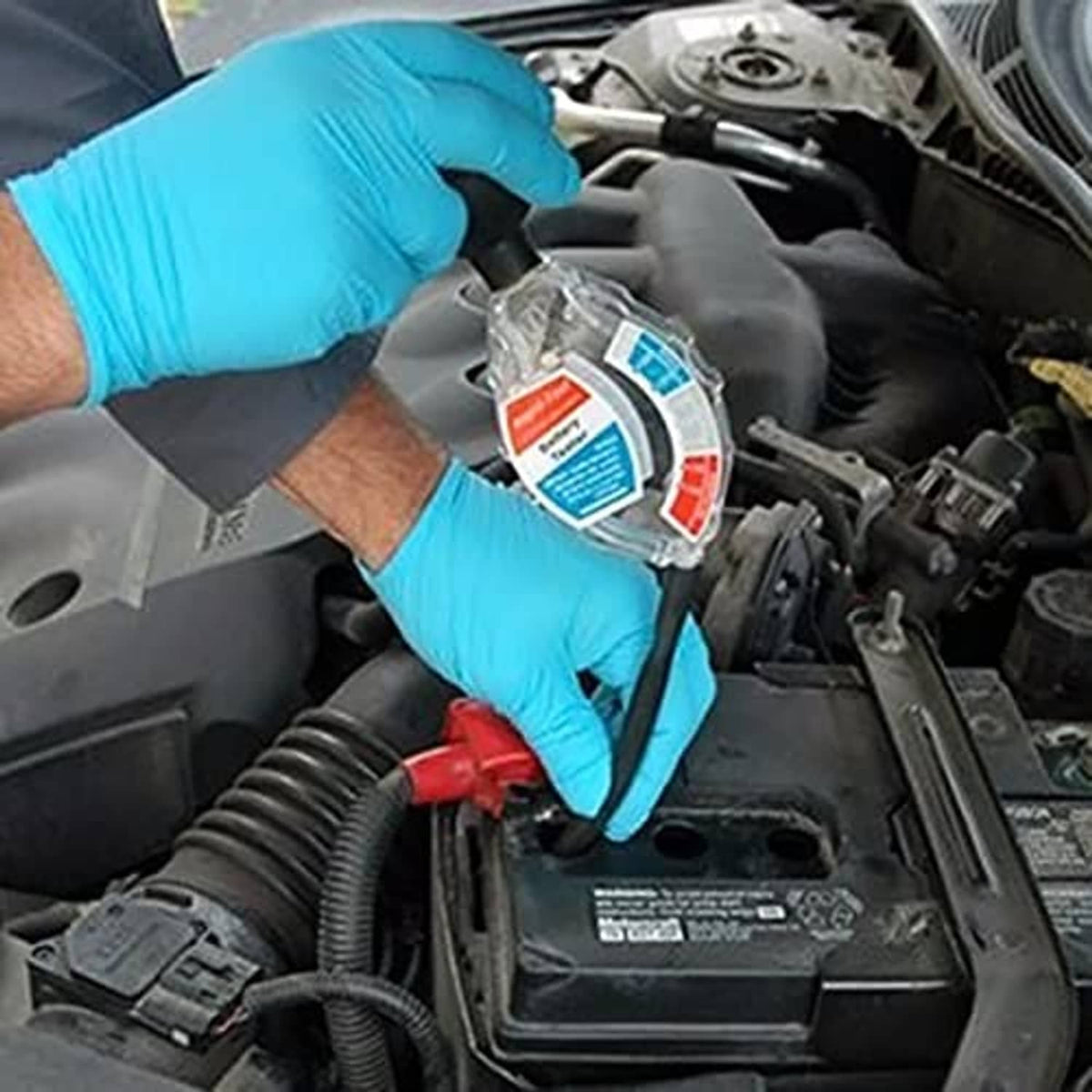 Battery hydrometer tester held by blue-gloved hands with black hose