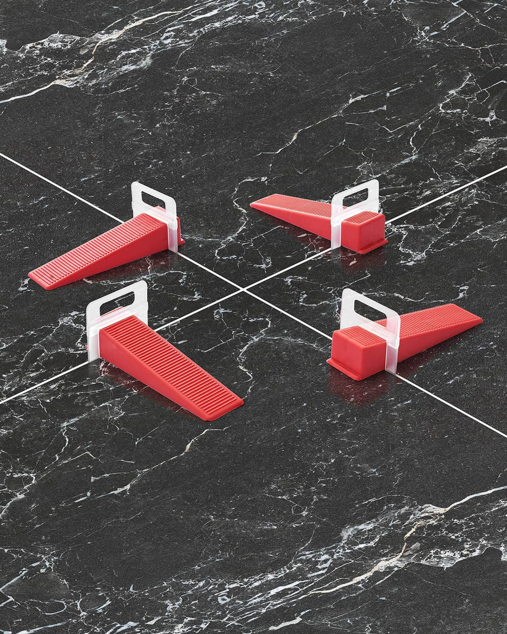 Red tile leveling spacer clips on dark floor tiles, holding tile edges evenly spaced