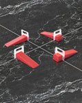 Red tile leveling spacer clips on dark floor tiles, holding tile edges evenly spaced