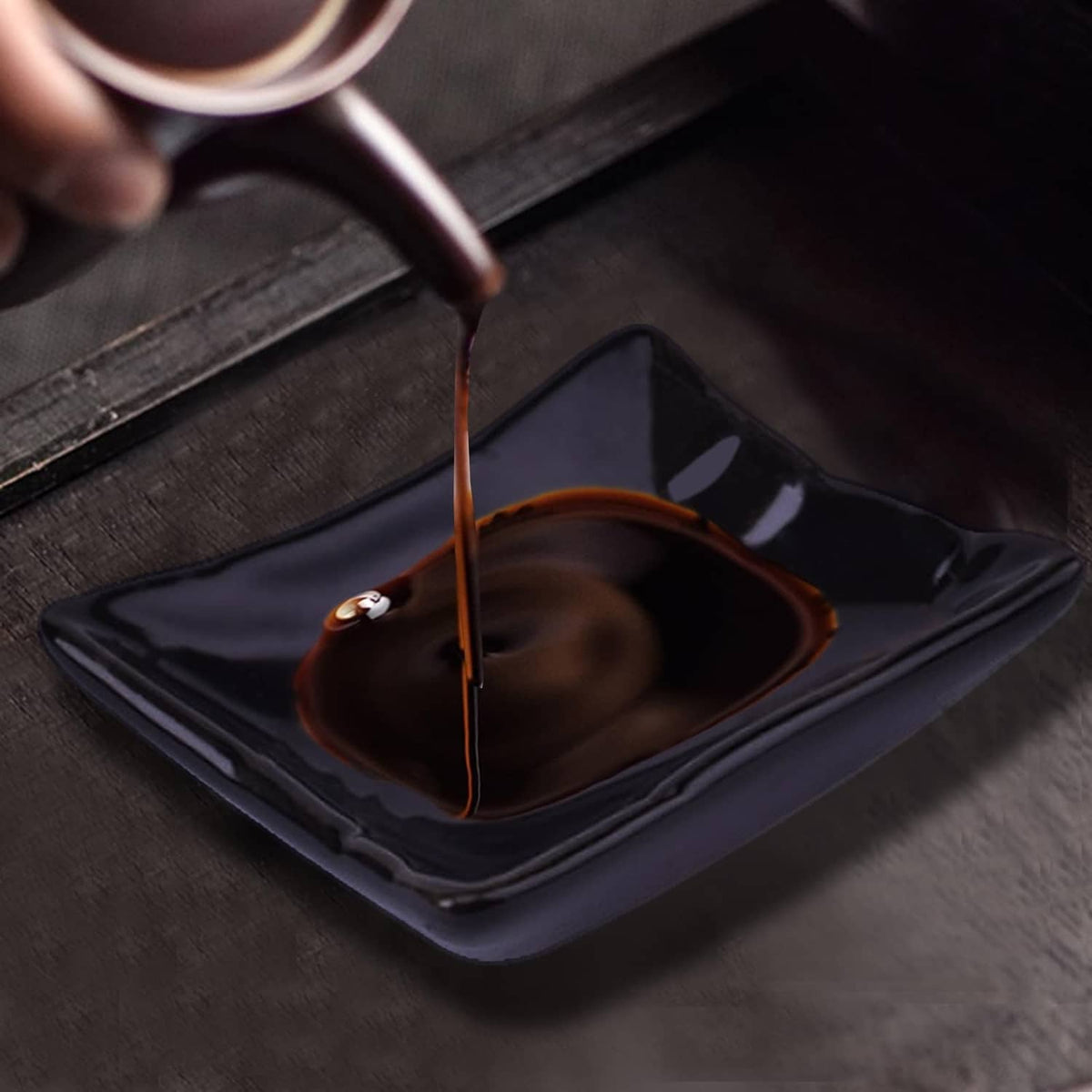 Square black soy sauce dish receiving brown sauce with chopsticks