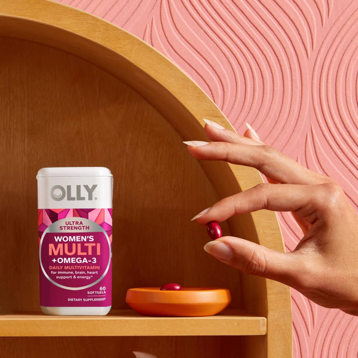 OLLY women’s multi softgels bottle with red capsules next to a container on shelf.