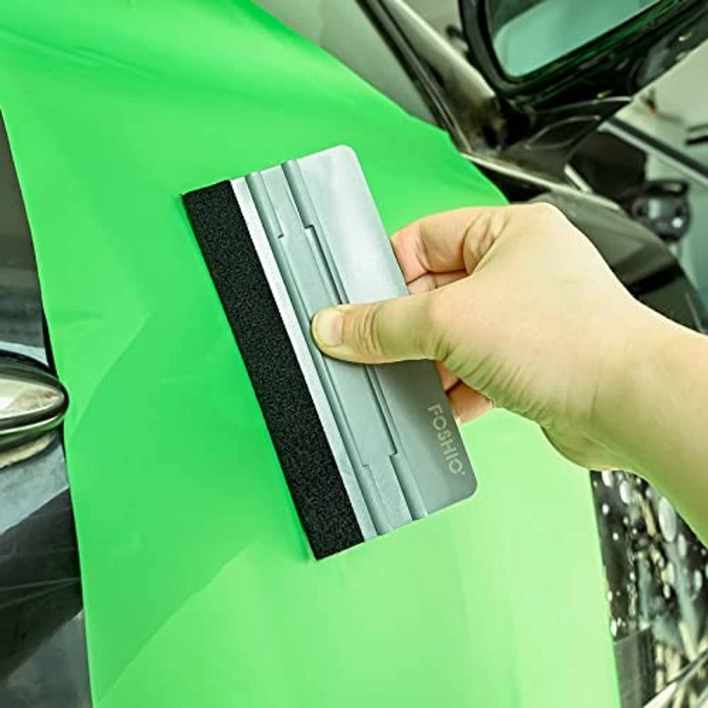 Hand uses gray felt squeegee on green film to apply window tint