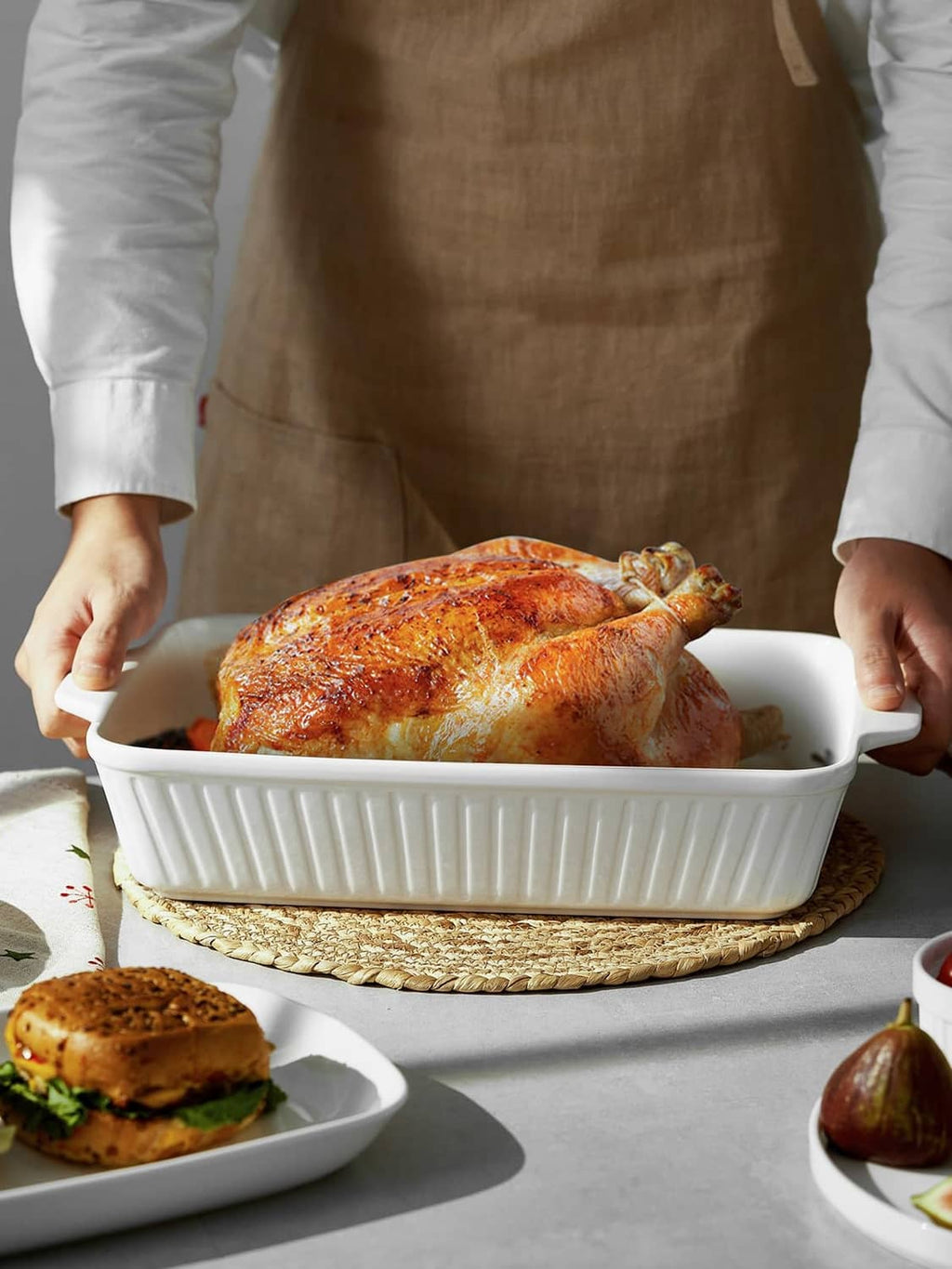 White ceramic casserole dish with two side handles, holding a roasted chicken.