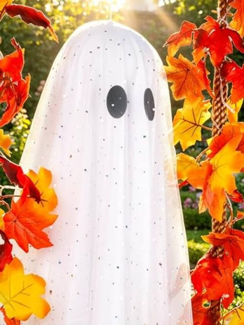 Close-up hanging ghost with speckled white fabric, black eyes, and red orange leaves