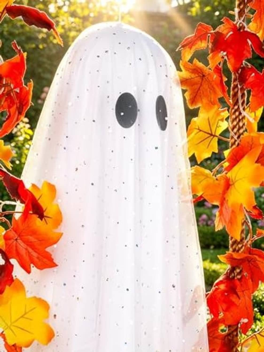 Close-up hanging ghost with speckled white fabric, black eyes, and red orange leaves