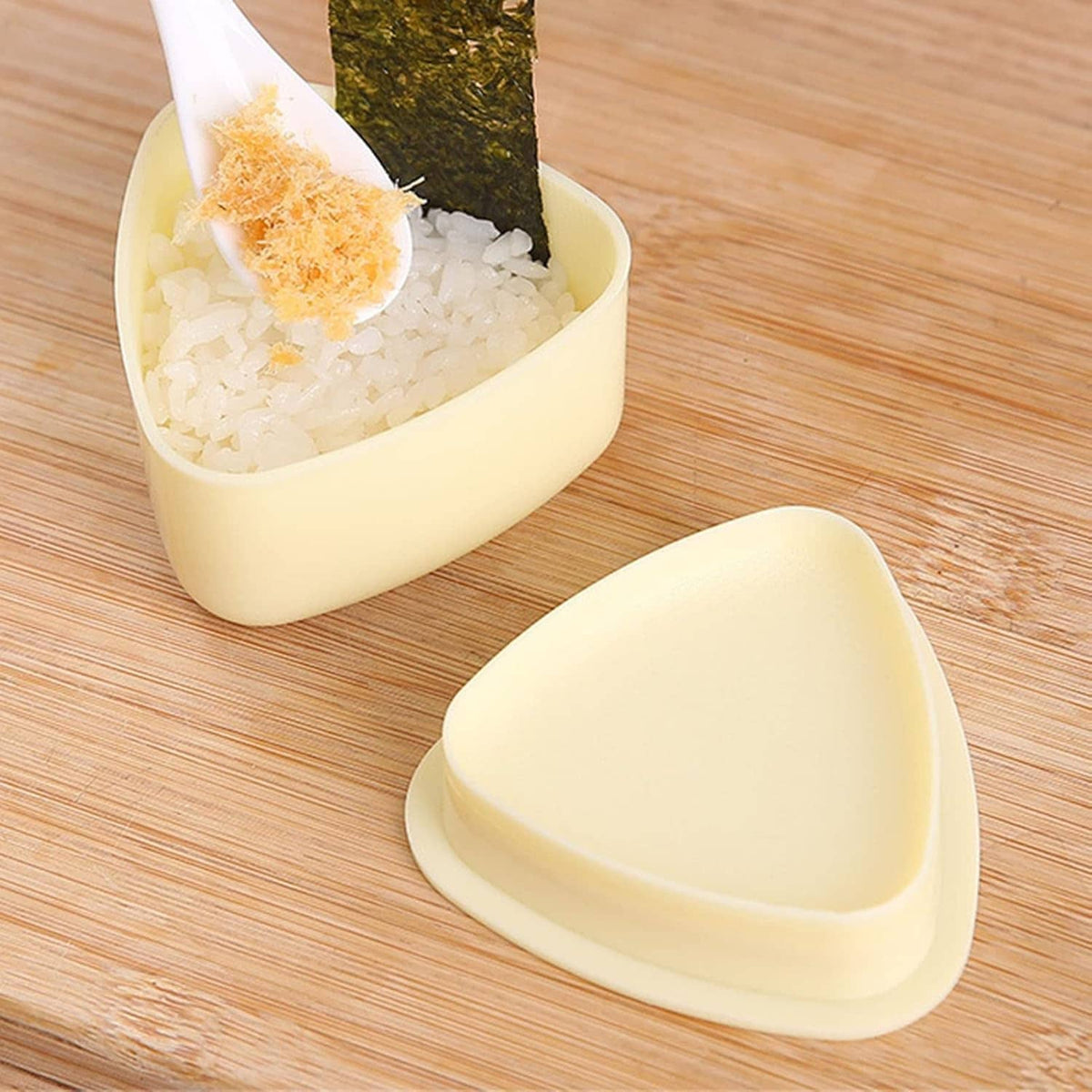Cream-yellow triangle onigiri press mold with rice inside and matching lid mold piece