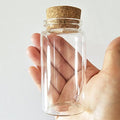 Small clear glass bottle vial with cork stopper, held in hand, cylindrical body