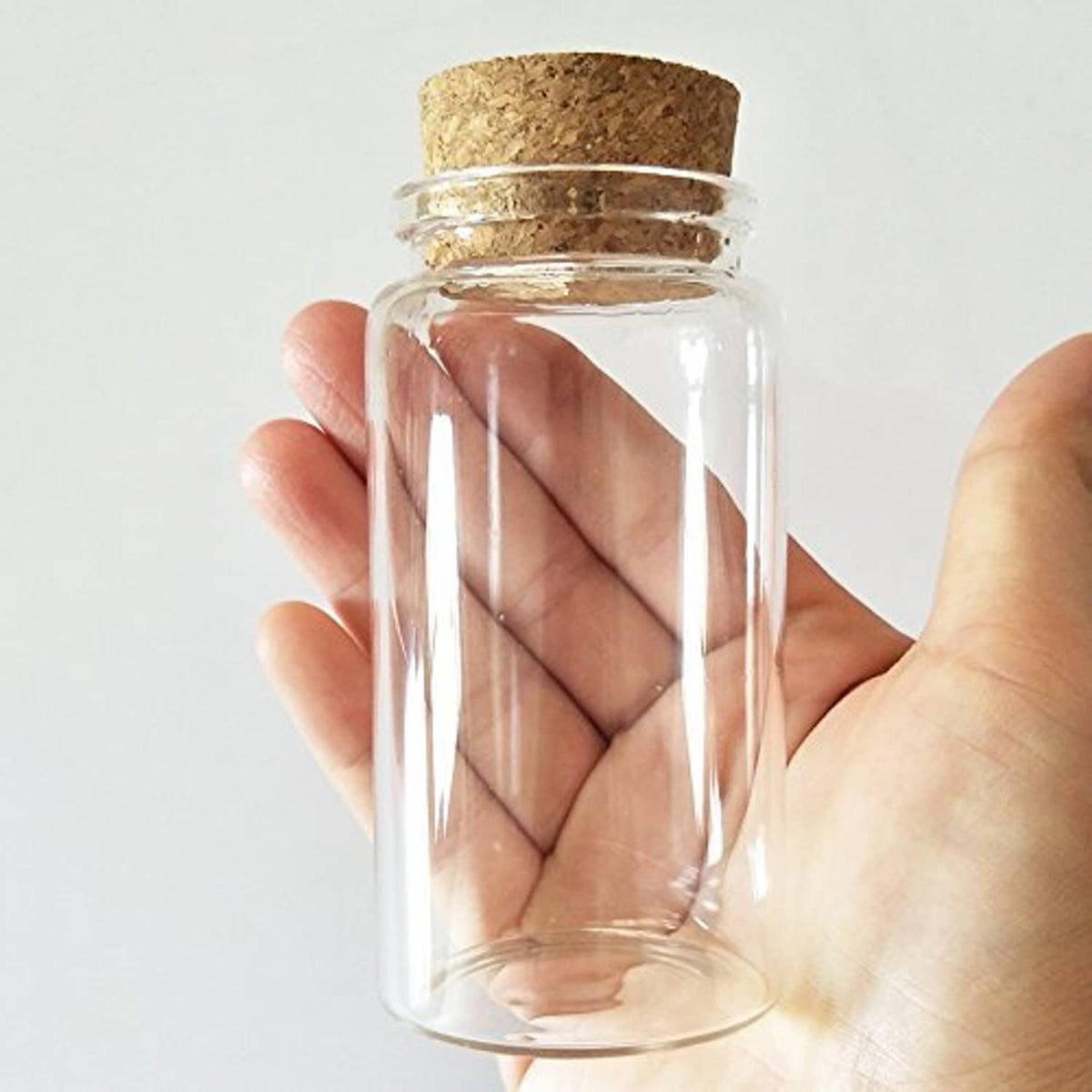 Small clear glass bottle vial with cork stopper, held in hand, cylindrical body