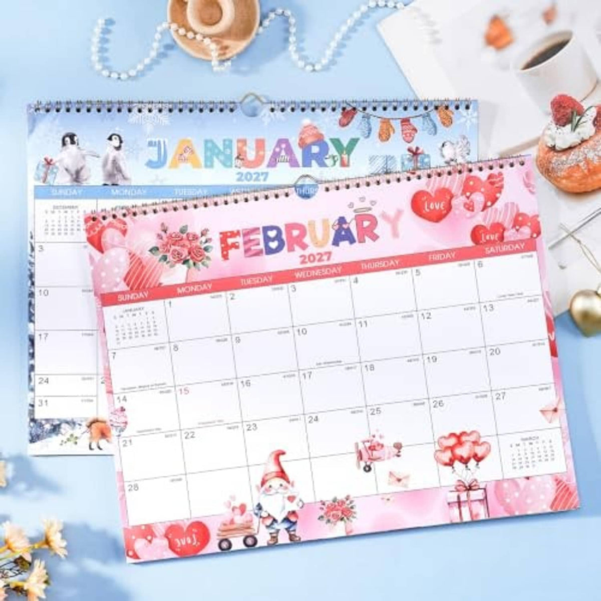 Wall calendar showing February 2027 page with pink hearts and gnome theme, spiral bound