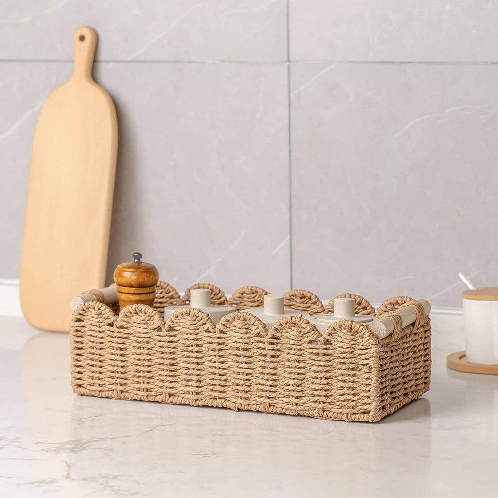 Scalloped woven rattan toilet paper basket on countertop with cups and paper rolls
