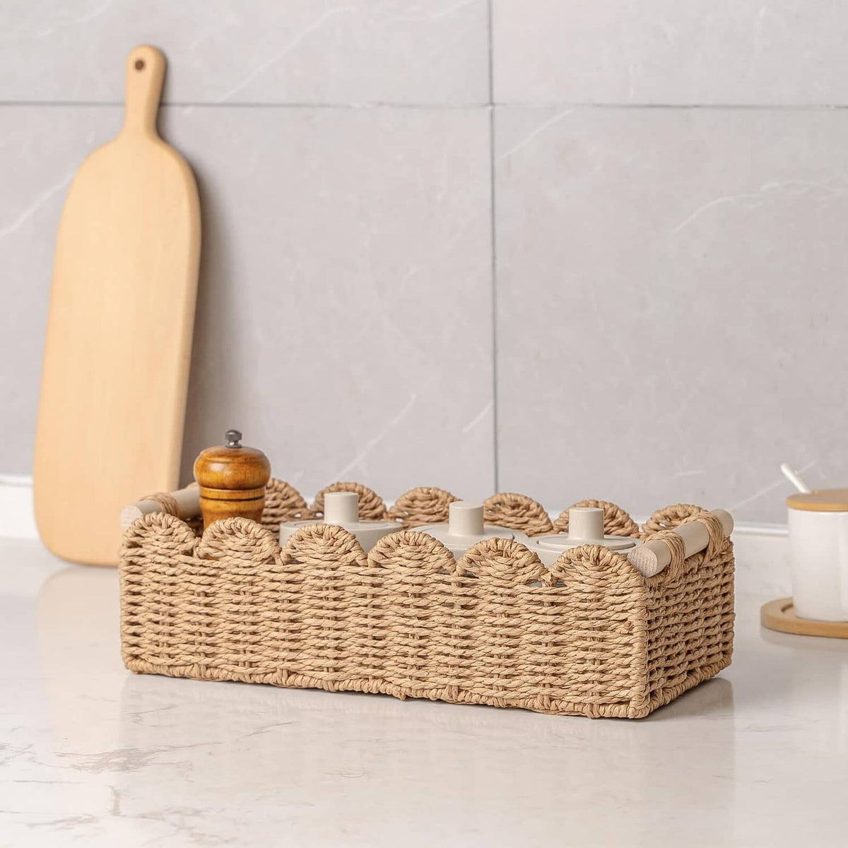Scalloped woven rattan toilet paper basket on countertop with cups and paper rolls