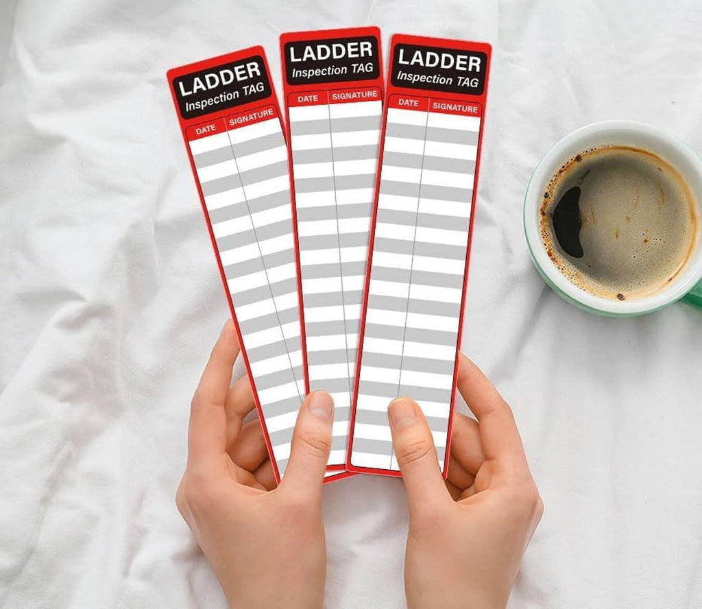 Pack of ladder inspection tag stickers held in hands, red borders and grey checklist