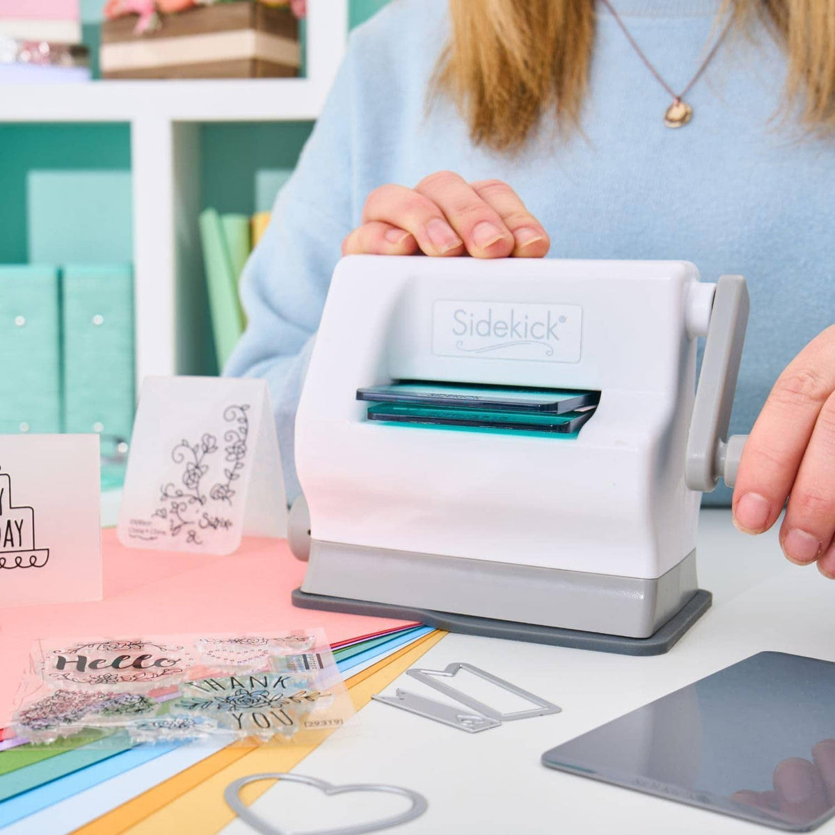 White manual die-cutting machine with teal plate, dies, and cardstock on work surface