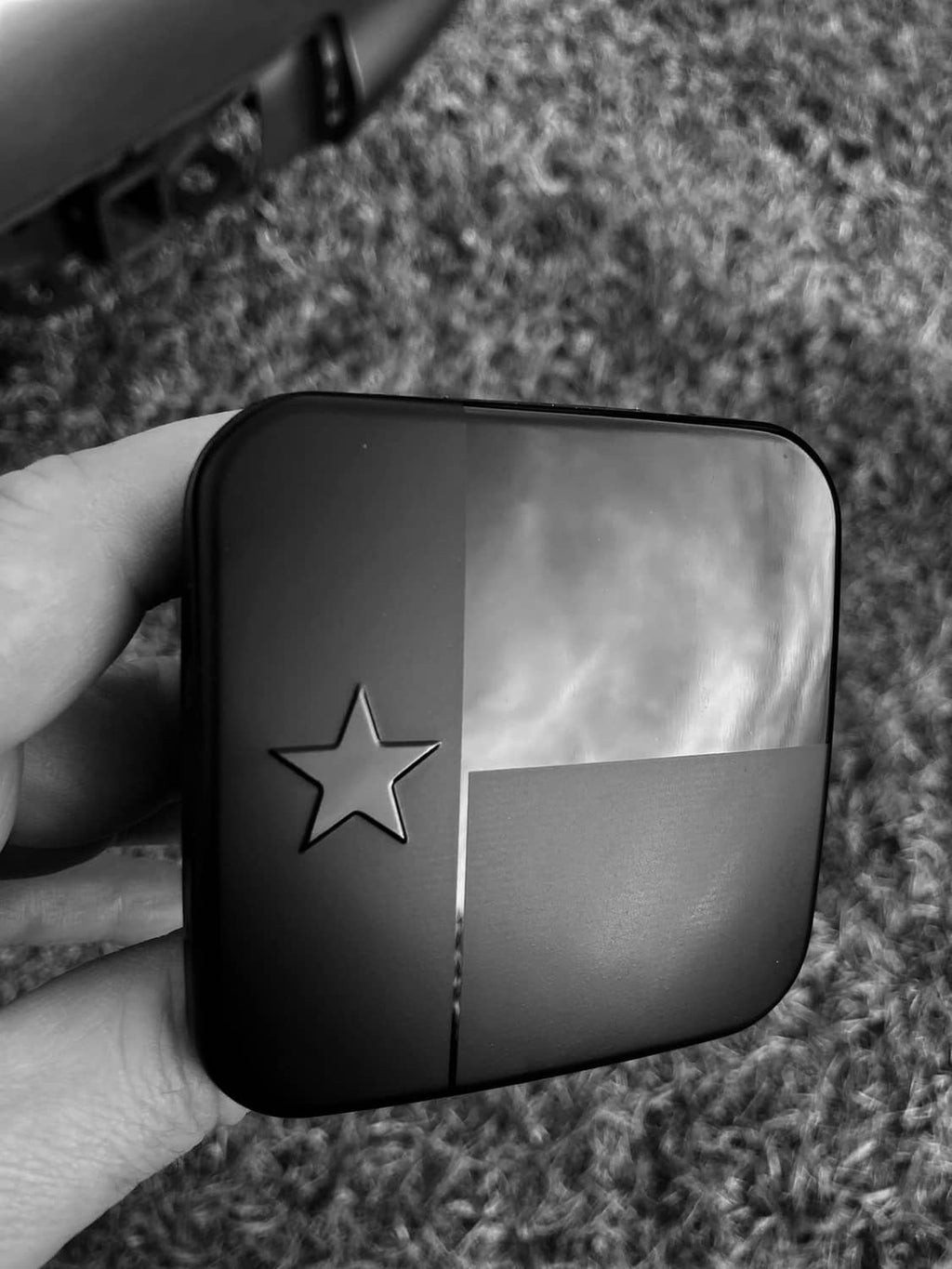 Black metal hitch cover plug with Texas star detail on glossy front panel.