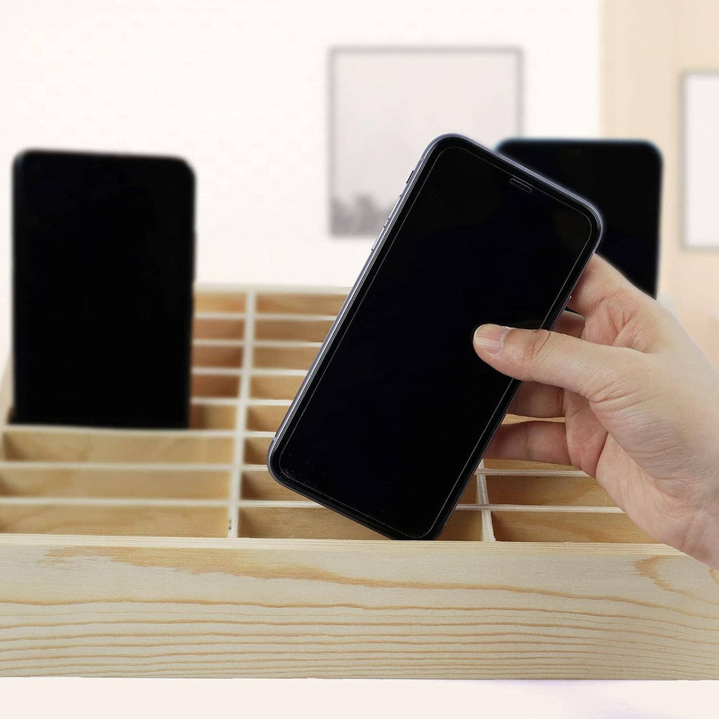 Hand placing a smartphone into a light wood 36-grid cell phone holder tray
