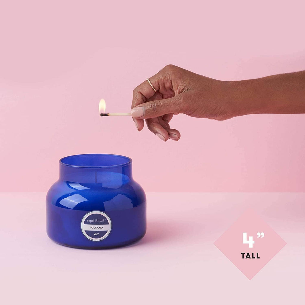 Blue glass jar candle with lit wick, hand holding a match above the jar