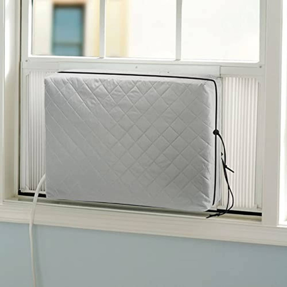 Grey quilted window AC unit cover with elastic straps and black securing cords.