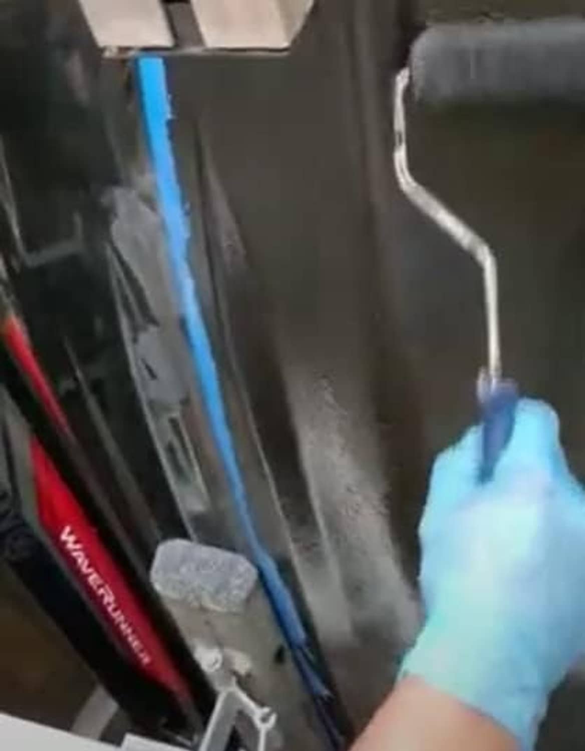 Gloved hand applying coating along a boat hull with a paint tool