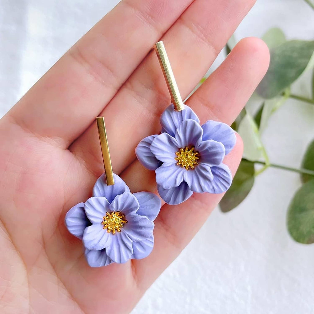 Blue flower polymer clay earrings on gold posts held in palm