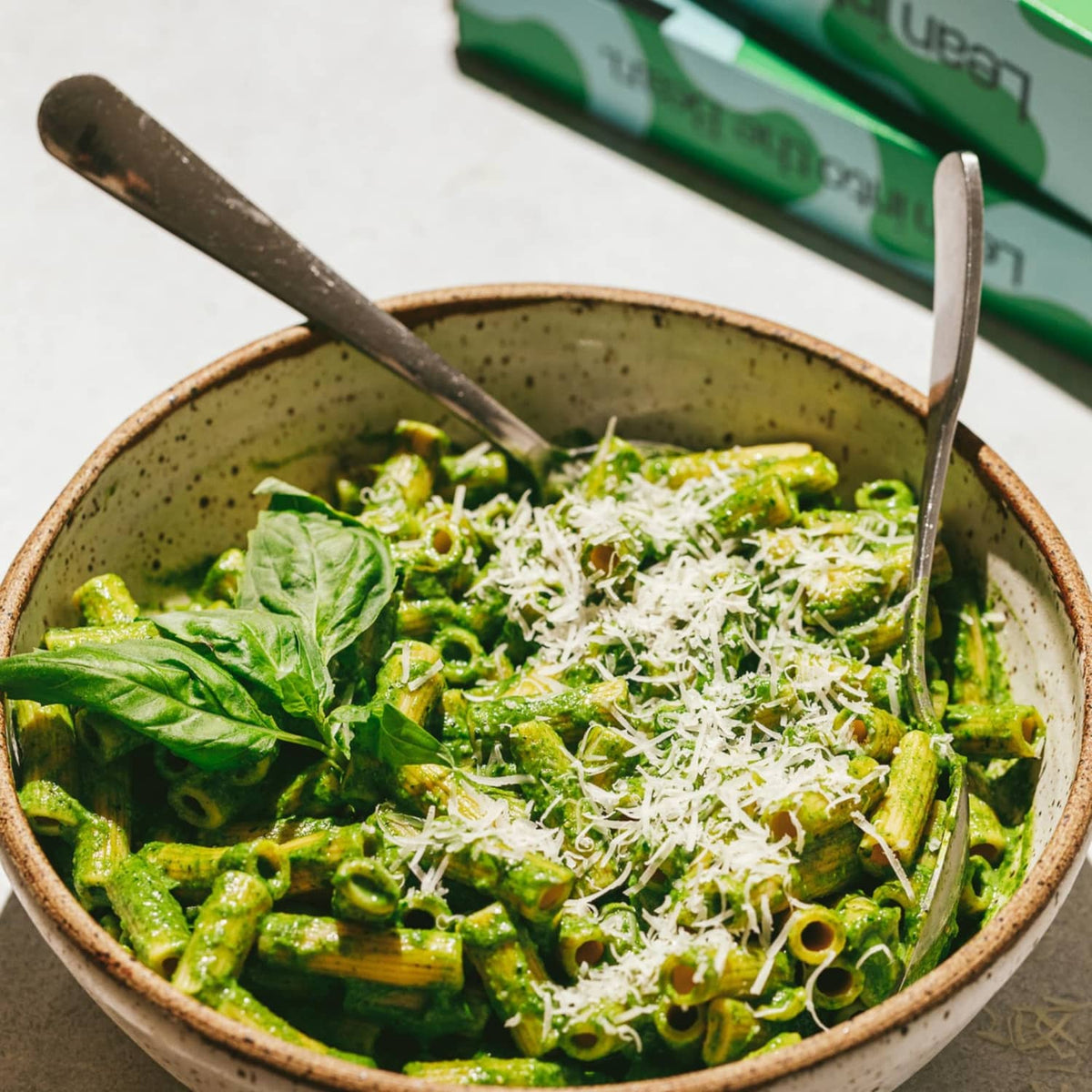 Green pasta bowl with spinach and broccoli, topped with grated cheese and herbs
